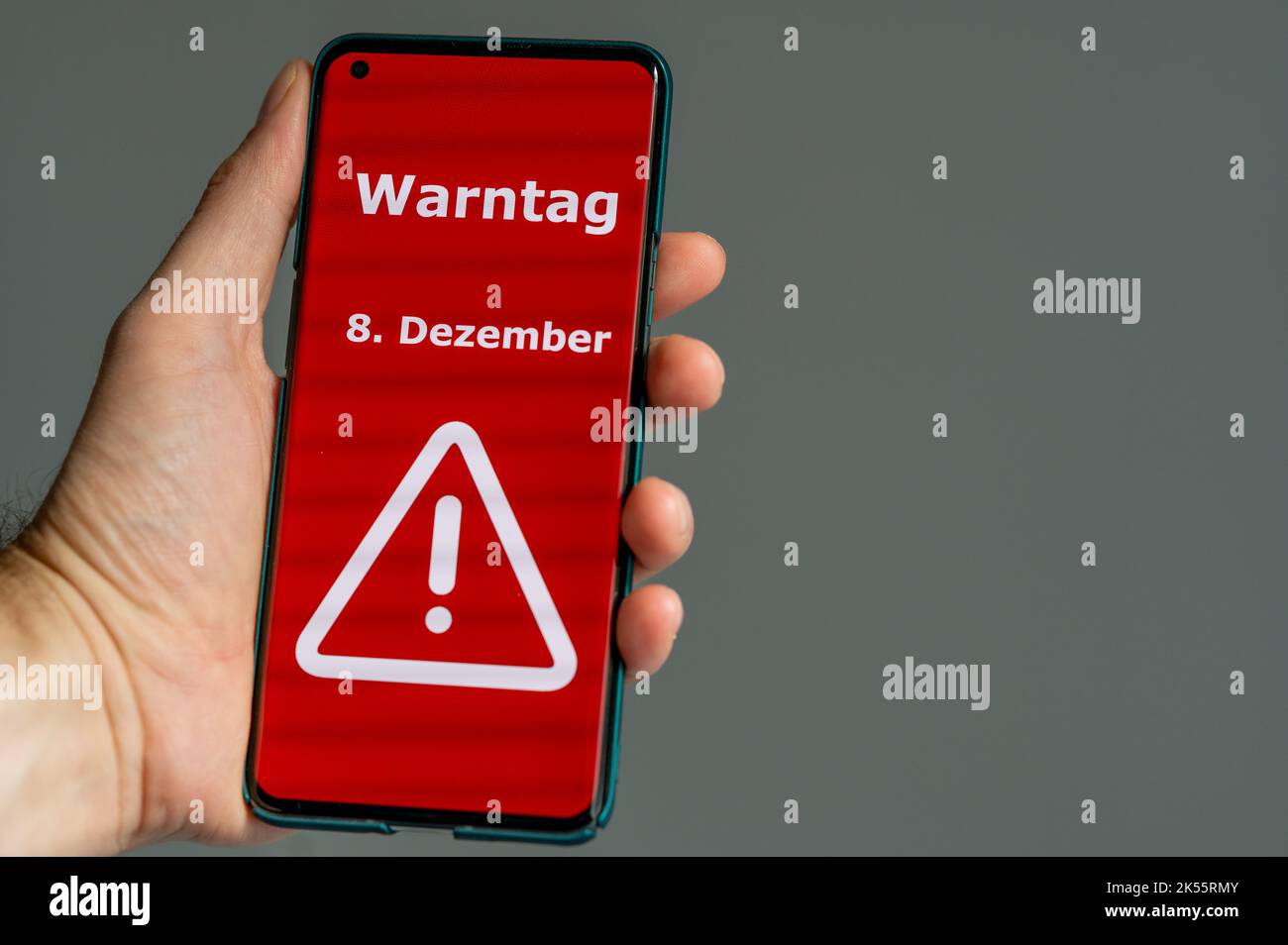 Simbolo della giornata nazionale di allarme in Germania 2022. La mano tiene un telefono cellulare con il testo tedesco 'Warntag 8. Dezember' (giorno di avvertimento il 8th dicembre Foto Stock