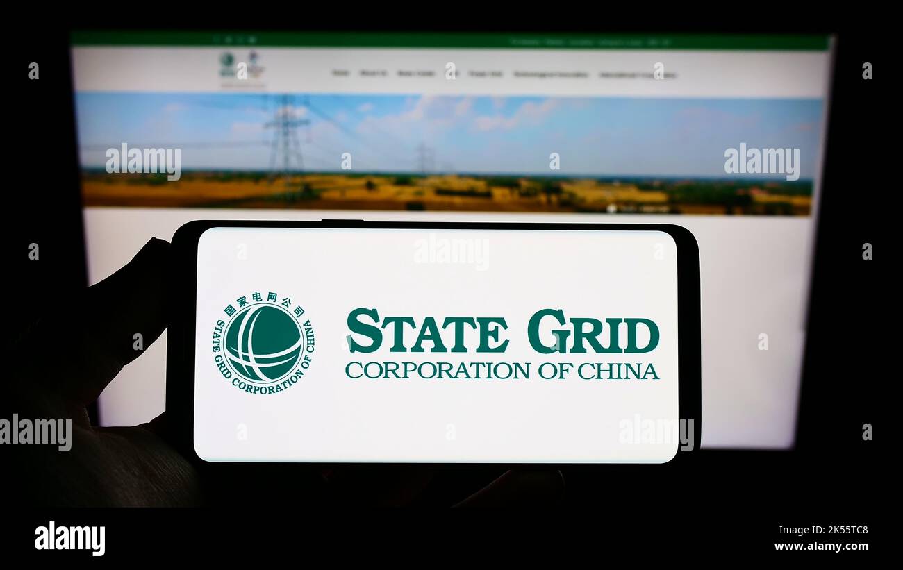 Persona che tiene in mano uno smartphone con il logo della società state Grid Corporation of China (SGCC) sullo schermo di fronte al sito Web. Messa a fuoco sul display del telefono. Foto Stock