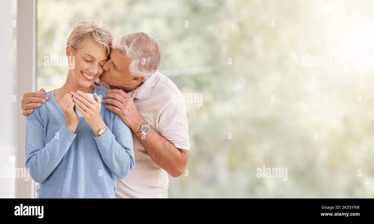 Caffè mattina, bacio e coppia anziana con sorriso durante la prima colazione in pensione presso la finestra con spazio mockup. Anziano uomo e donna con amore Foto Stock