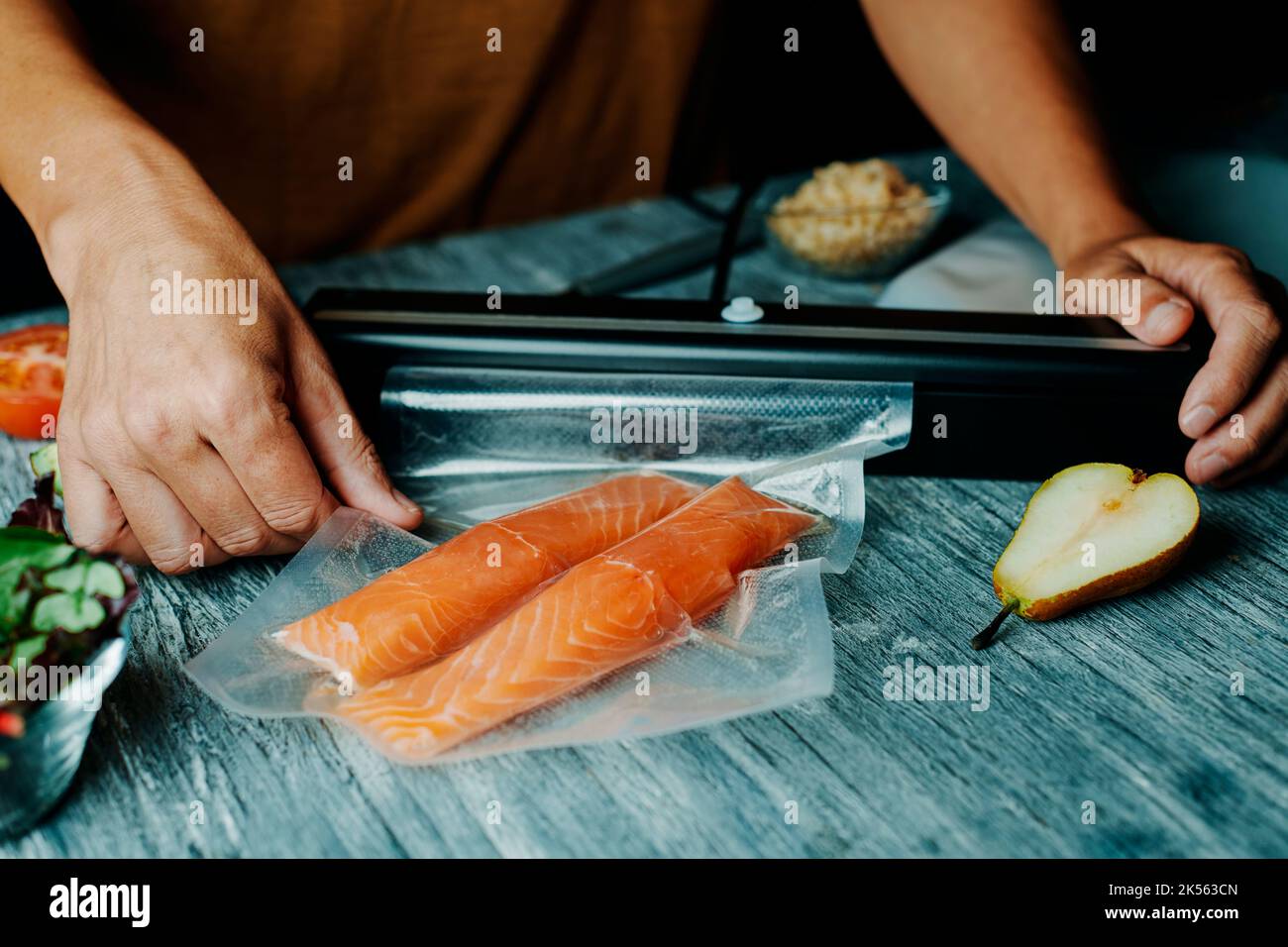 primo piano di un giovane uomo che confezionerà sotto vuoto due pezzi di salmone in un sacchetto sottovuoto, su un tavolo grigio rustico Foto Stock