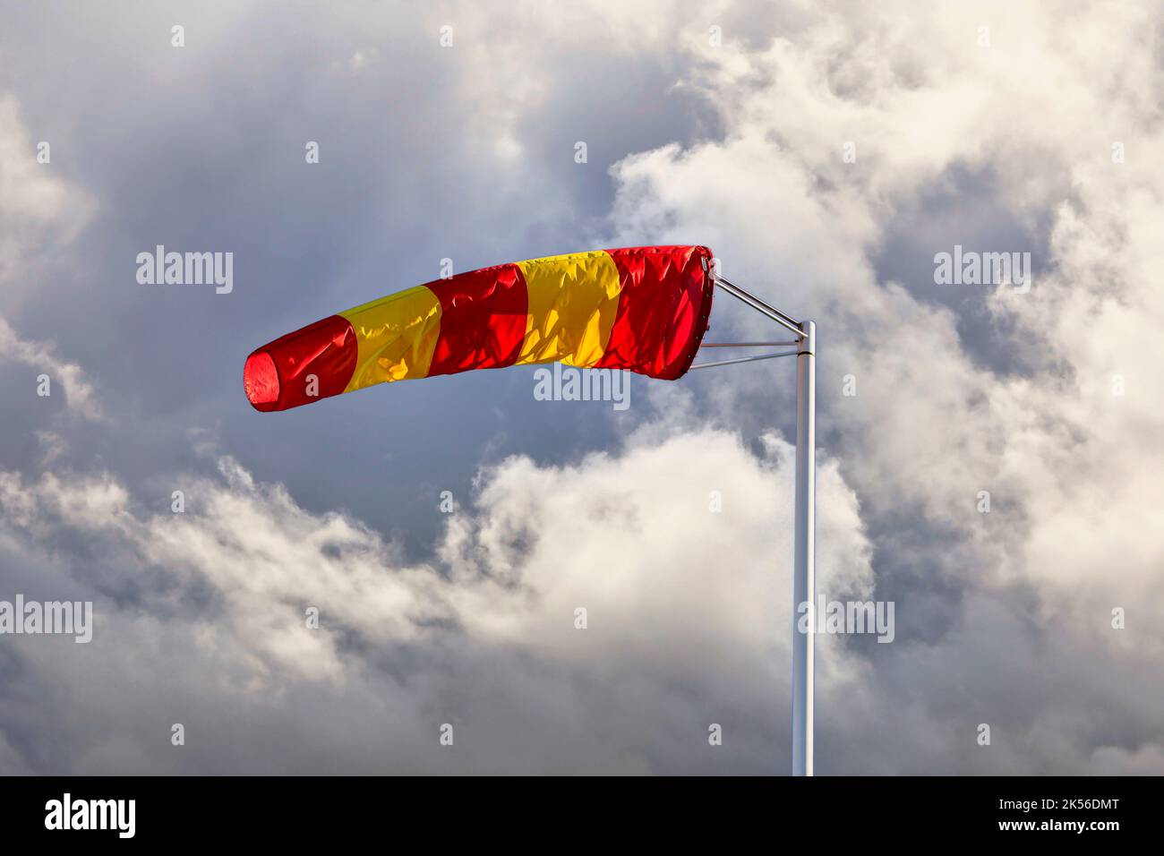 Calza a vento a righe gialle e rosse o cono del vento contro cielo nuvoloso scuro, che indica la direzione e la forza del vento. Copiare lo spazio per il testo. Foto Stock