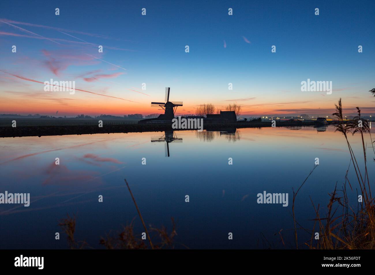 Mulino a vento "Adermolen' al tramonto con riflesso nell'acqua sul canale Ringvaart in Abbenes, Paesi Bassi. Foto Stock