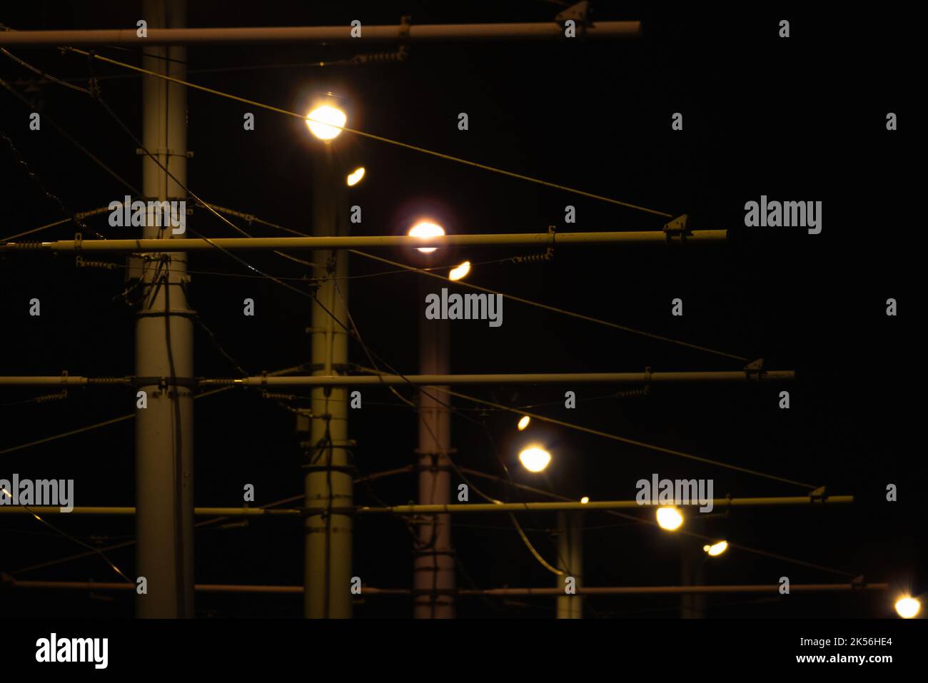 Le luci della strada e i fili del tram sono sullo sfondo del cielo scuro. Foto astratta della notte urbana Foto Stock