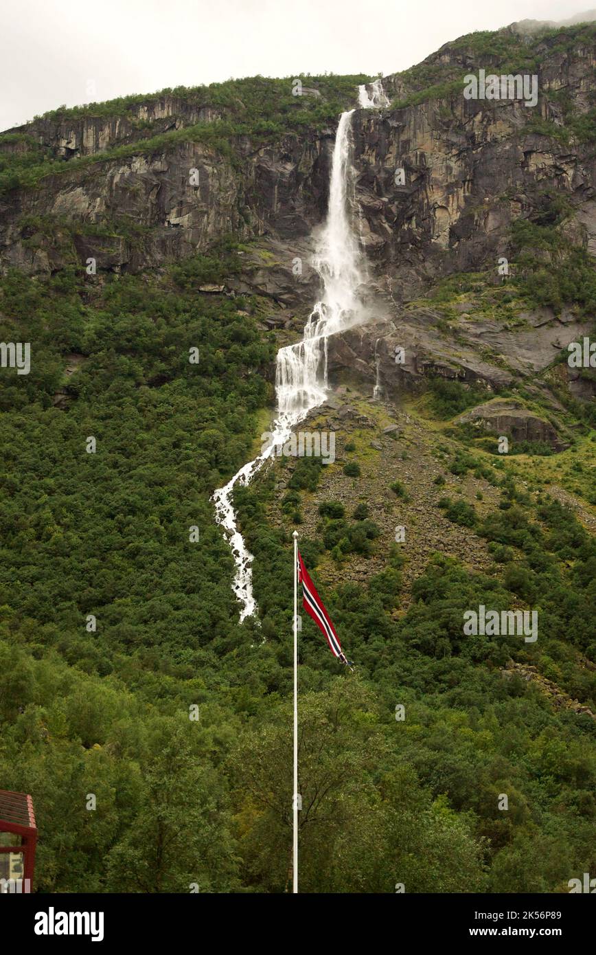 Bandiera norvegese (pennon) che soffia nel vento, con una cascata sullo sfondo. Montagne a Briksdalsbreen, Jostedalsbreen. Norvegia pennant / pendente. Foto Stock