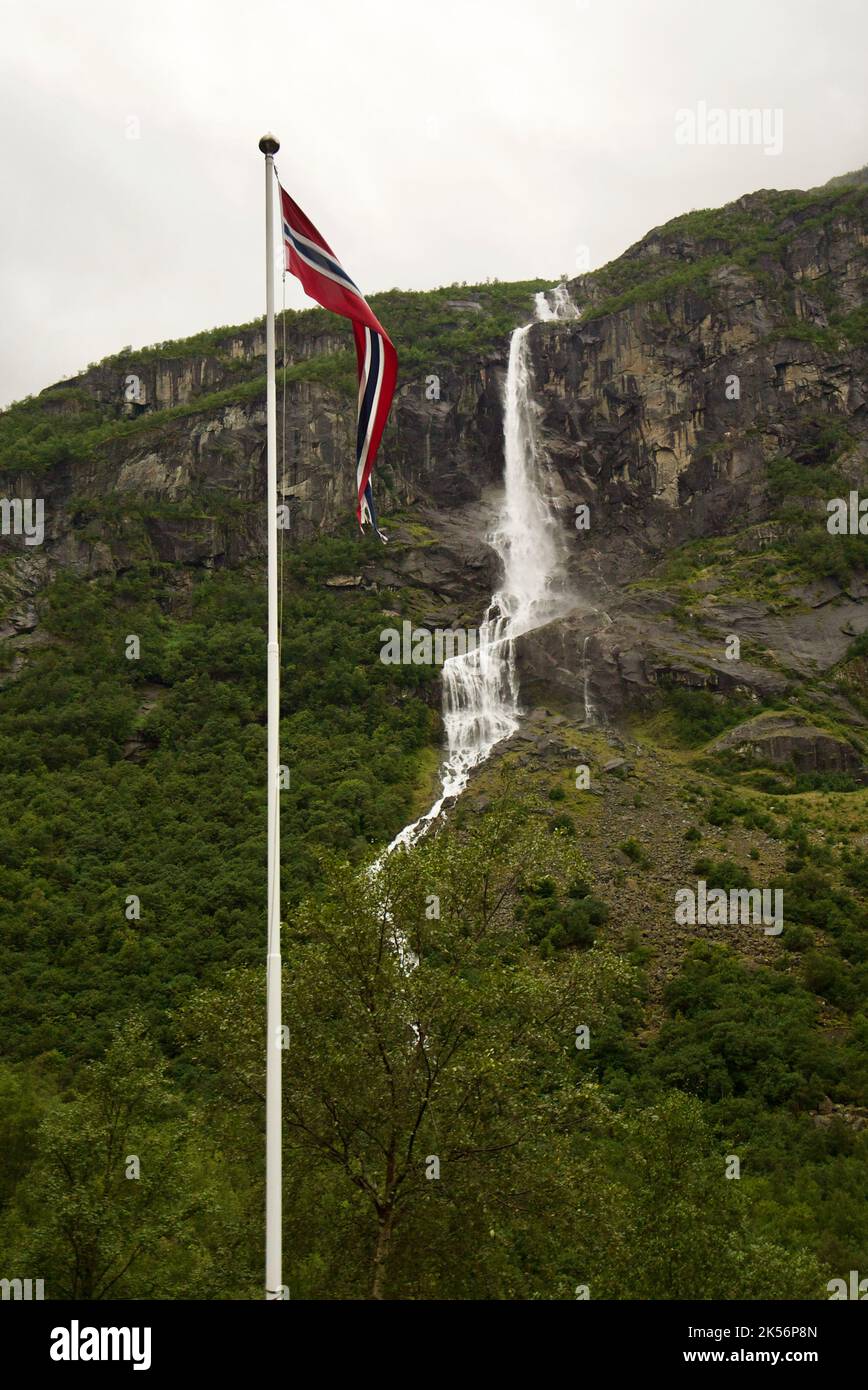 Bandiera norvegese (pennon) che soffia nel vento, con una cascata sullo sfondo. Montagne a Briksdalsbreen, Jostedalsbreen. Norvegia pennant / pendente. Foto Stock