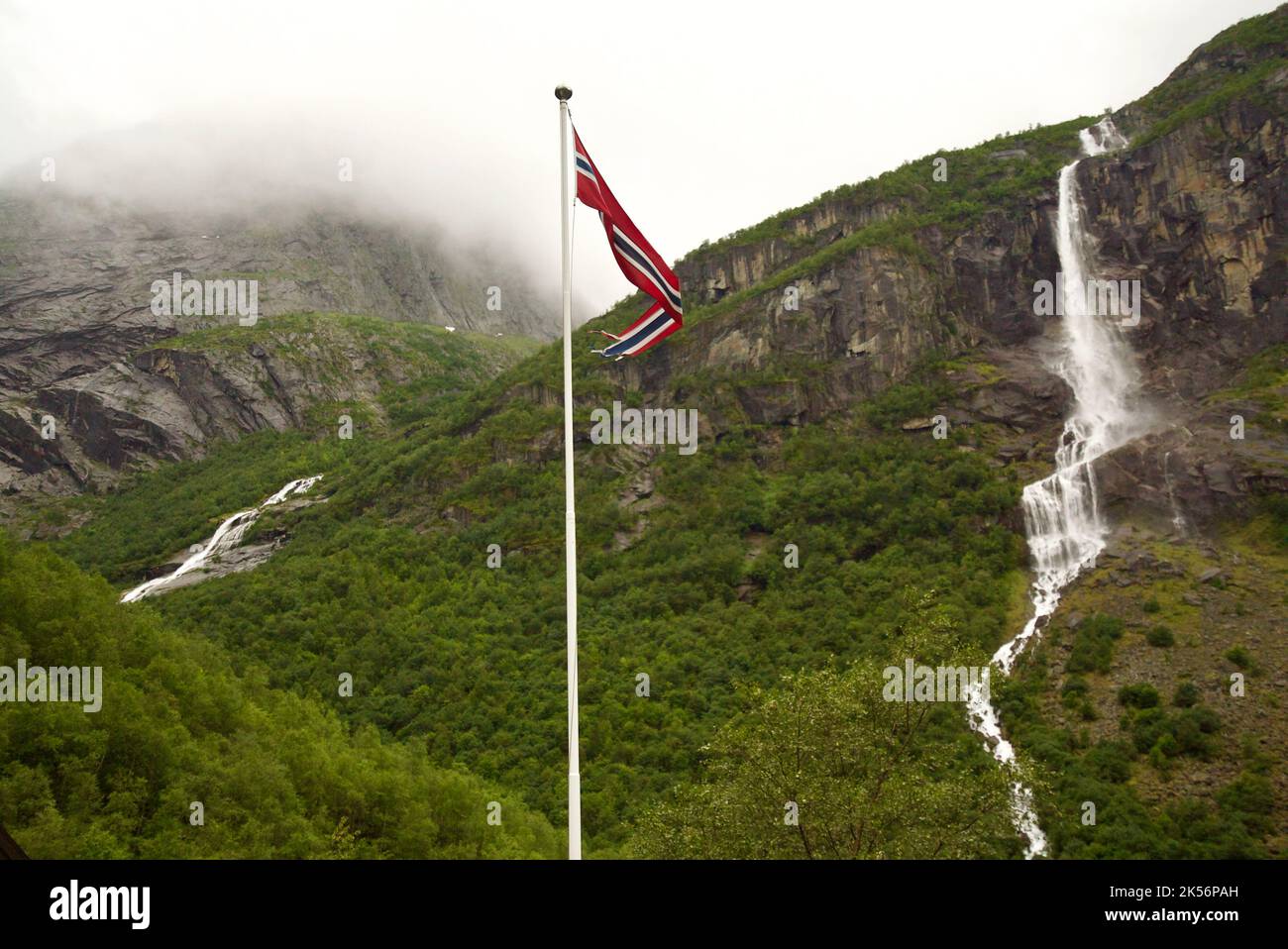 Bandiera norvegese (pennon) che soffia nel vento, con una cascata sullo sfondo. Montagne a Briksdalsbreen, Jostedalsbreen. Norvegia pennant / pendente. Foto Stock