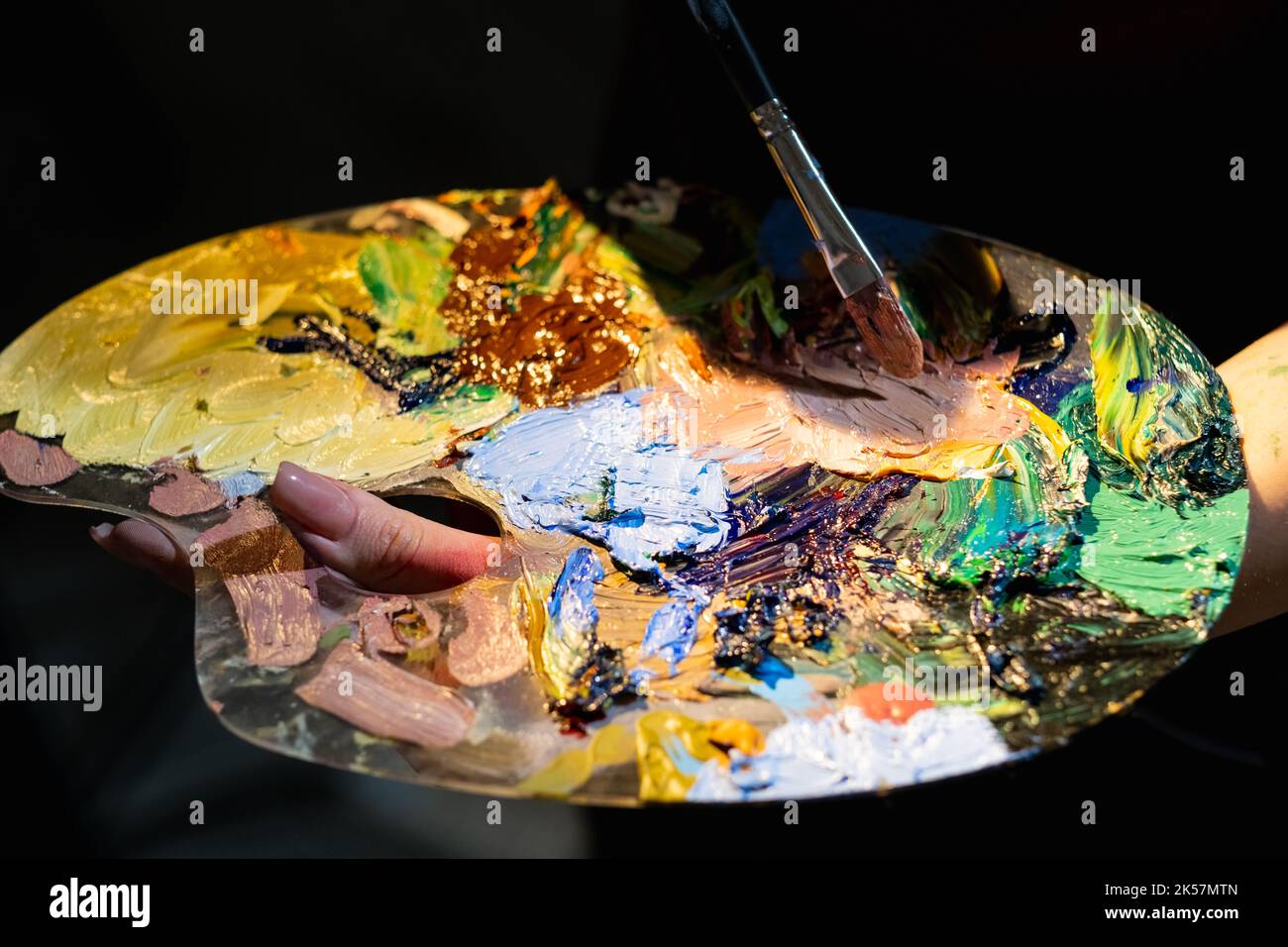 Durata del colore. Processo creativo. Strumenti artistici. Pittura grafica. Donna irriconoscibile che tiene la tavolozza con la fusione di colori pitture e pennello isolato scuro. Foto Stock
