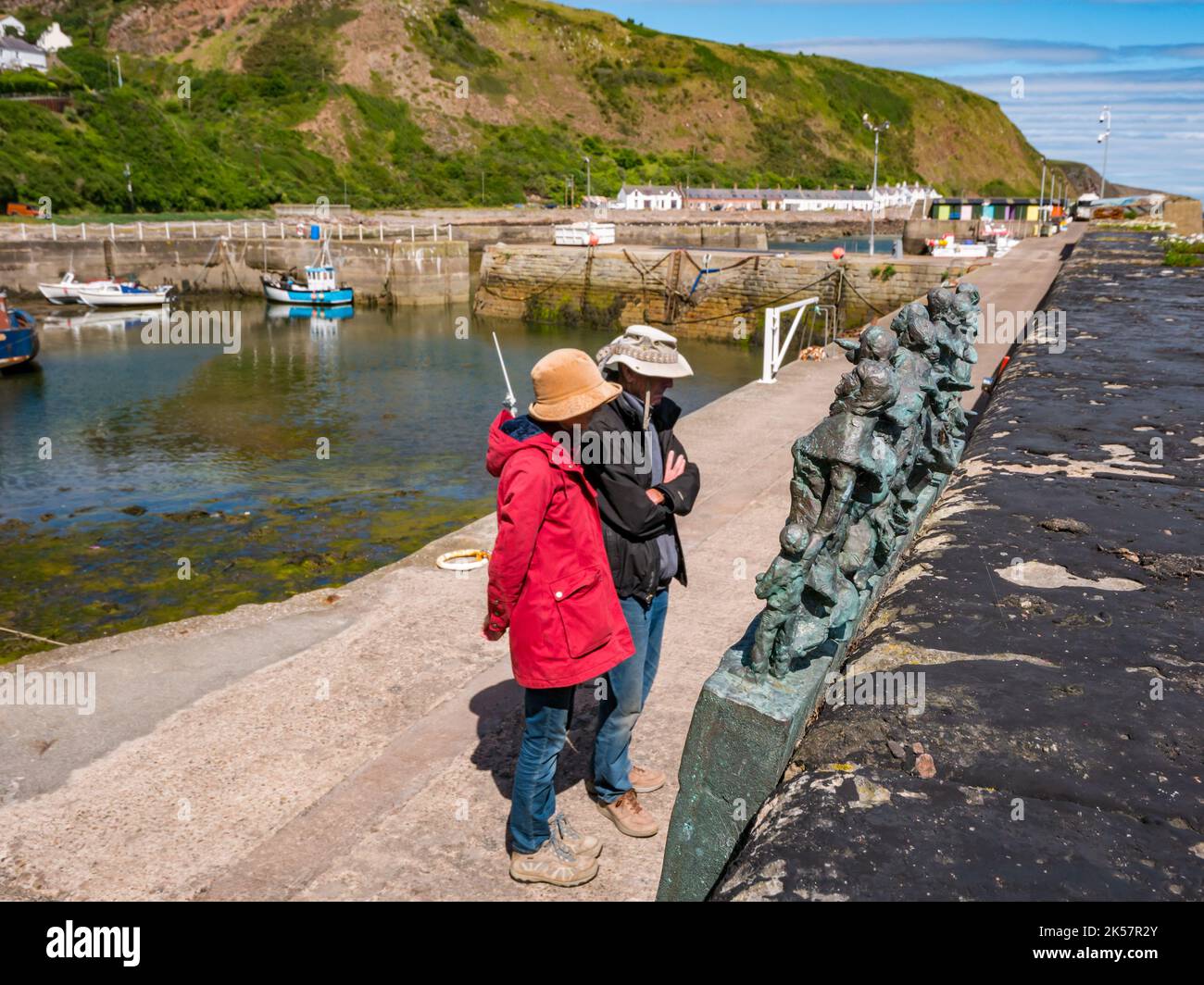 Coppia anziana che guarda la scultura commemorativa in bronzo del disastro della pesca del 1881, il porto di Burnmouth, Berwickshire, Scozia, Regno Unito Foto Stock