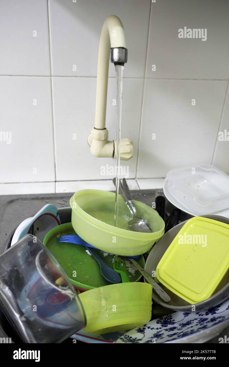 piatti sporchi nel lavandino con acqua che scorre dal rubinetto Foto Stock