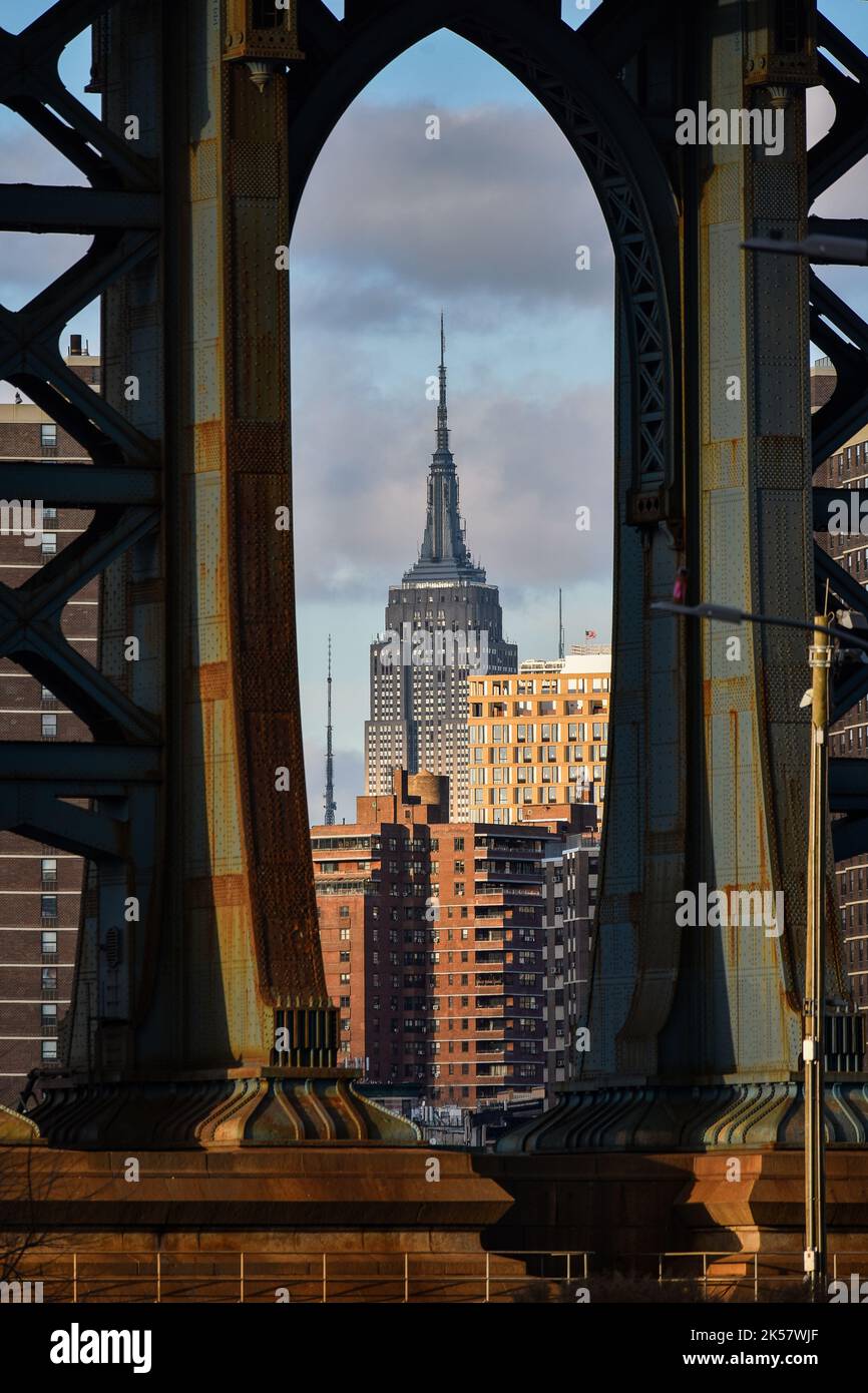 Vista dell'edificio statale dell'impero circondato da edifici attraverso un pilone del ponte di Manhattan al tramonto. Foto Stock