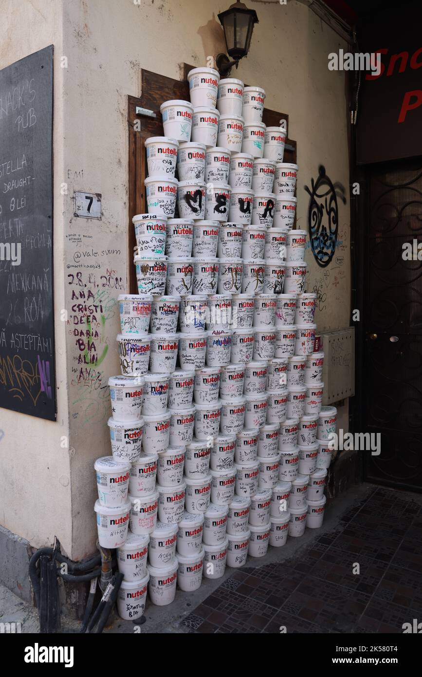 Torre di contenitori di Nutella usati con testi scritti su di essi, accatastati contro un muro; concetto di sovradosaggio di Nutella Foto Stock