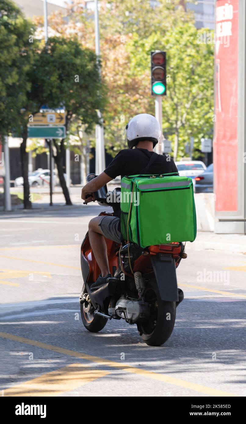 Consegna cibo moto scooter autista con zaino verde dietro la schiena è sulla sua strada per consegnare il cibo. Corriere su scooter Foto Stock