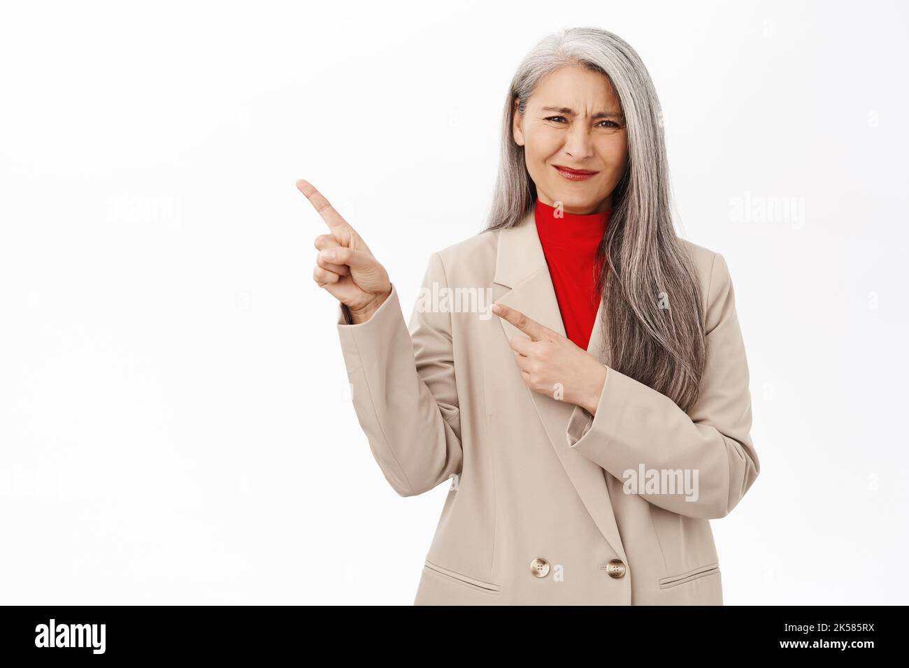Donna d'affari anziana asiatica, imprenditore femminile che punta a sinistra con volto deluso, in piedi sconvolto contro sfondo bianco Foto Stock