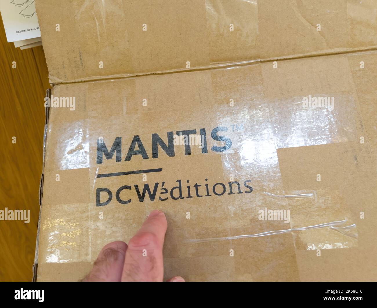 Parigi, Francia - 9 aprile 2022: POV maschio mano unboxing puntando al cartone con il logotipo DCW Edizioni e Mantis lampada al suo interno - creato da Schottlander nel 1951 Foto Stock