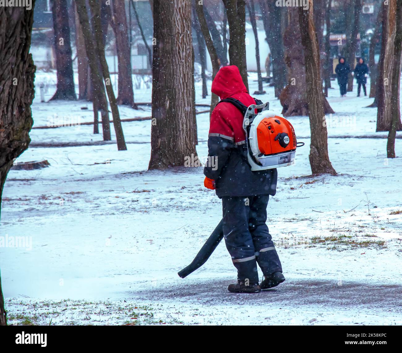 Dnepropetrovsk, Ucraina - 02.04.2022: Lavoro stagionale delle utenze cittadine nel parco. Un lavoratore con una soffiante motorizzata zaino soffia la neve da un parco pa Foto Stock Dnepropetrovsk, Ucraina - 02.04.2022: Lavoro stagionale delle utenze cittadine nel parco. Un lavoratore con una soffiante motorizzata zaino soffia la neve da un parco pa Foto Stock
