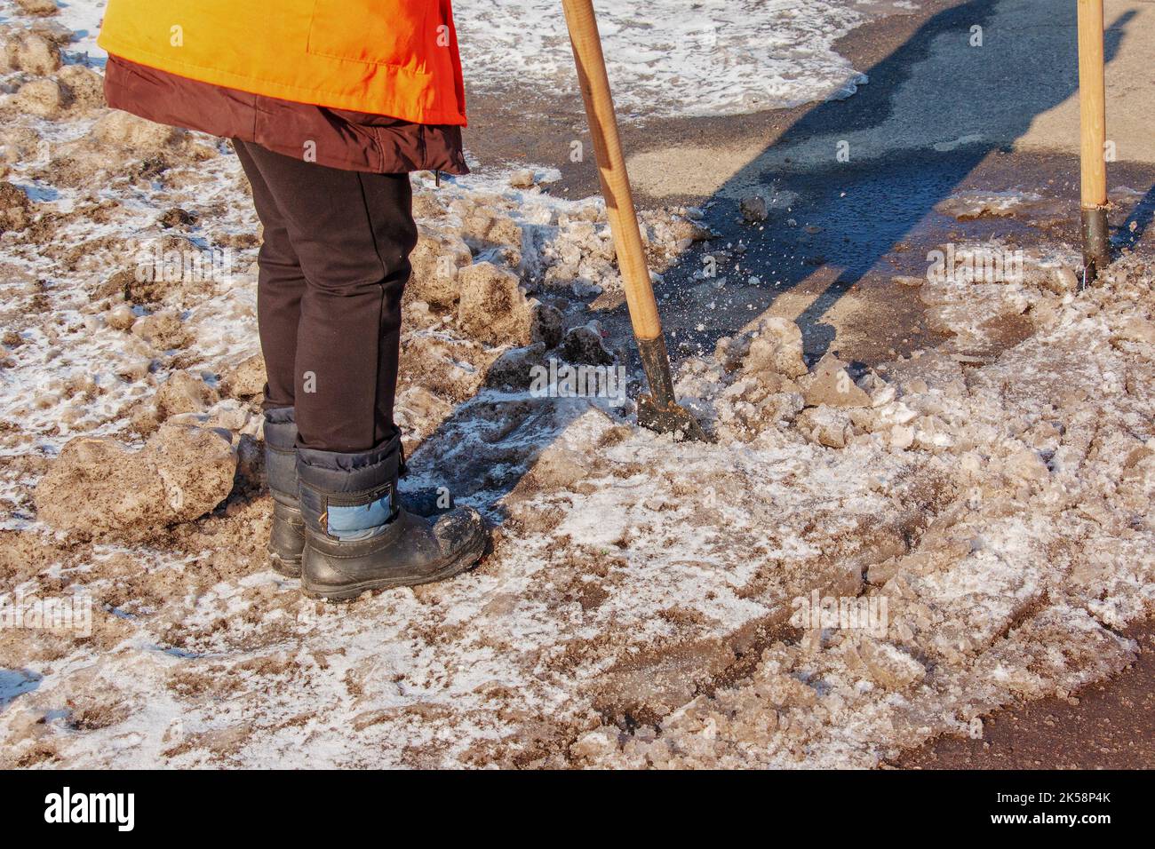 Una donna operatrice pulisce il ghiaccio e rimuove la neve dalle lastre di pavimentazione utilizzando un rompighiaccio. Un uomo rompe il ghiaccio con un frantoio a lame d'acciaio, anche un rompighiaccio Foto Stock