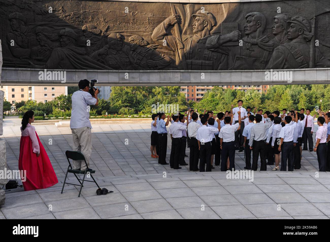 08.08.2012, Corea del Nord, Pjoengjang - Un gruppo di studenti nordcoreani si trova sotto un gigantesco rilievo di bronzo al monumento alla fondazione del lavoratore Foto Stock