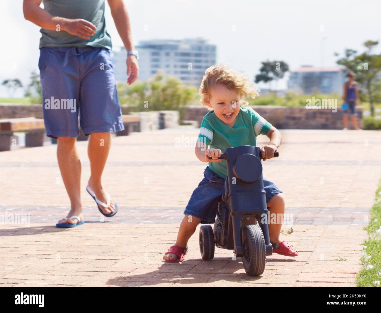 HES nato per essere un ragazzo biker. Un ragazzo felice del bambino che cavalca è moto giocattolo fuori mentre il suo padre corre dietro lui. Foto Stock