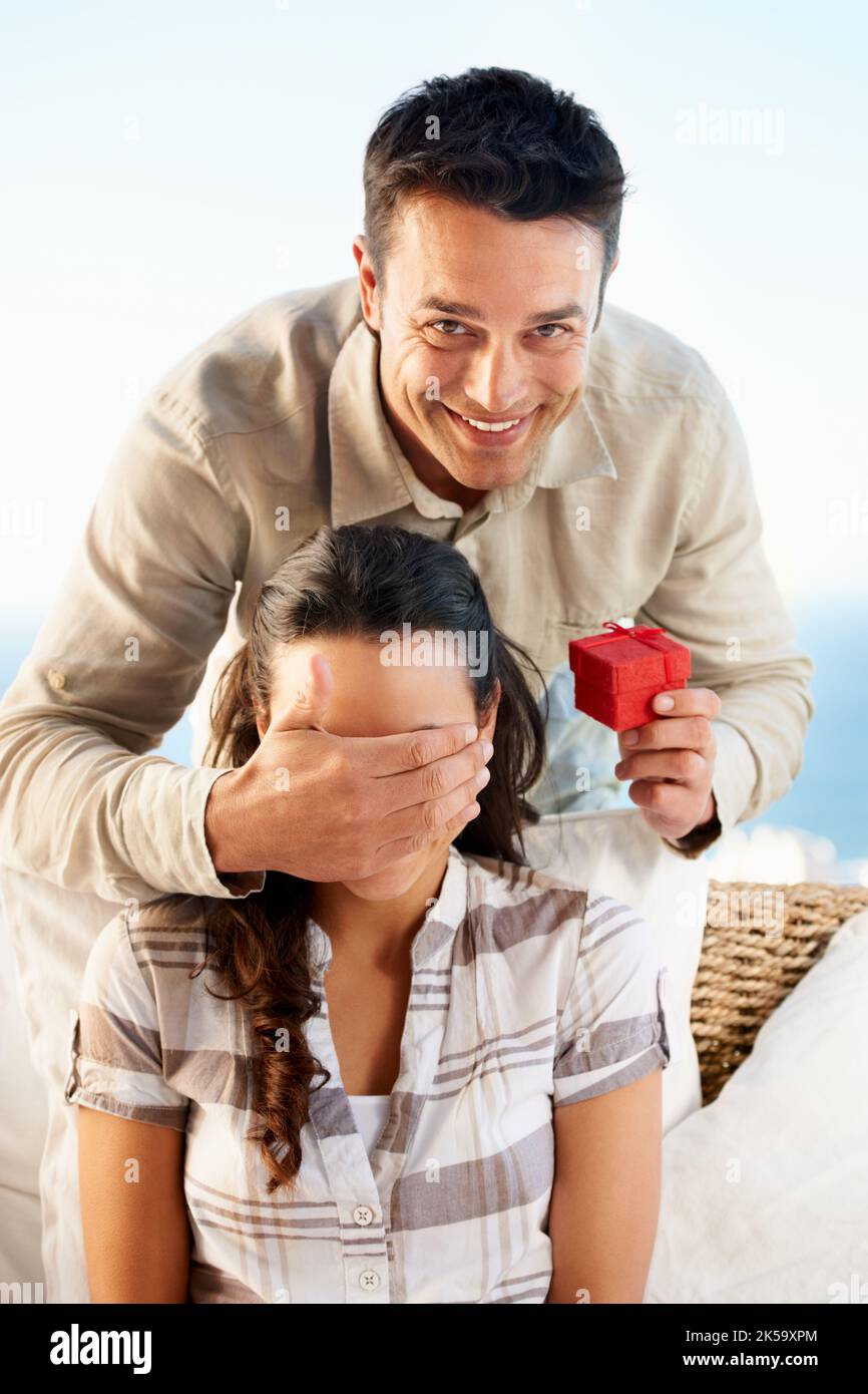Non ha idea di cosa sta venendo. Un giovane che tiene una scatola dell'anello con la mano sugli occhi delle sue fidanzate. Foto Stock