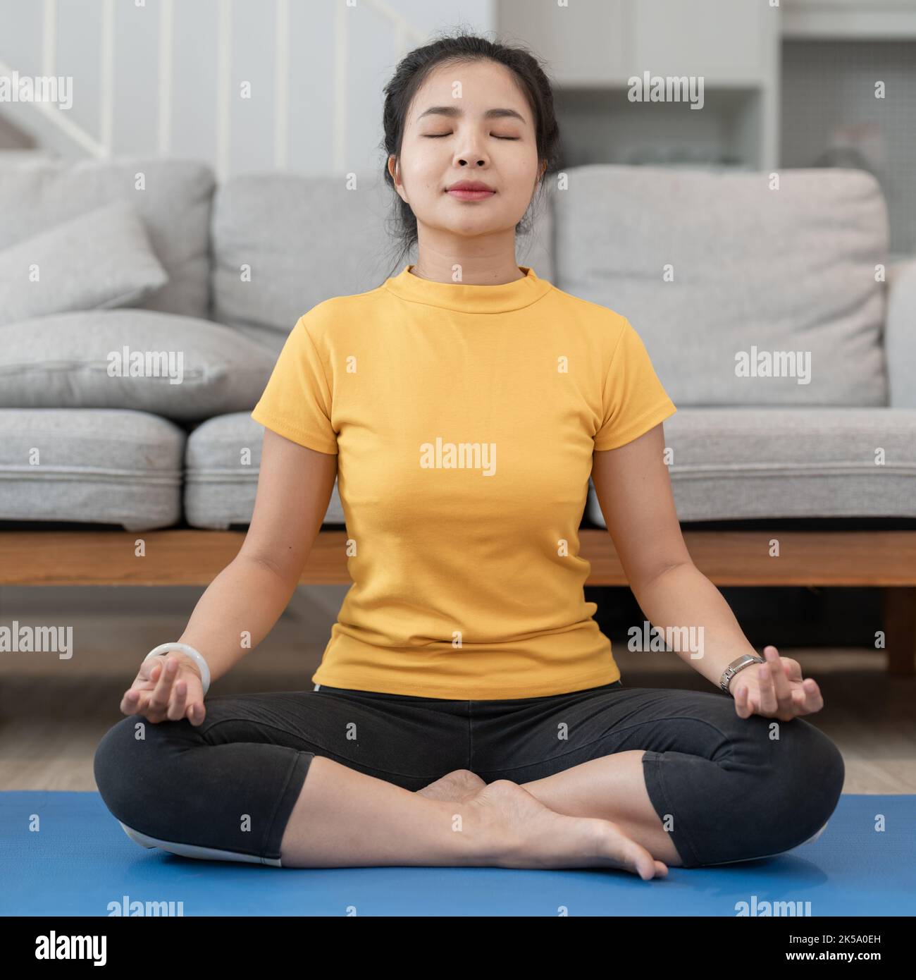 Giovane donna asiatica che fa esercizio di yoga in casa, meditando. Rapporto quadrato. Foto Stock