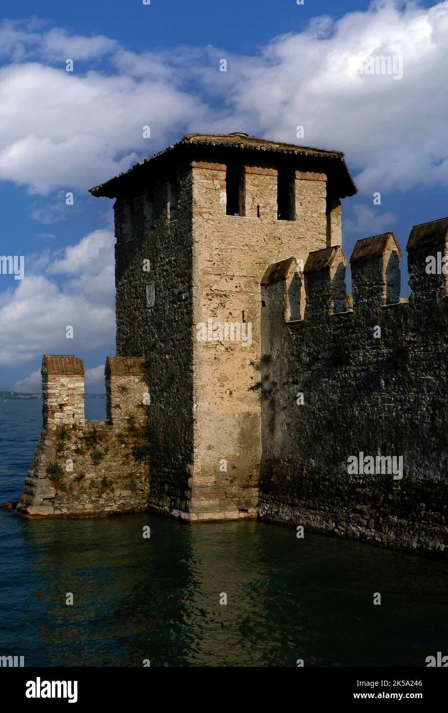 A Sirmione sul Lago di Garda in Lombardia, in Italia, mura battute e una torre di guardia sorvegliano la foce di un porto fortificato medievale annesso al Castello Scaligero o alla Rocca Scaligera. Costruito nel 1300, il castello prende il nome dalla famiglia della Scala, dinastia regnante di Verona, che dominava la zona all'epoca. È una delle fortezze scaligere meglio conservate. Foto Stock