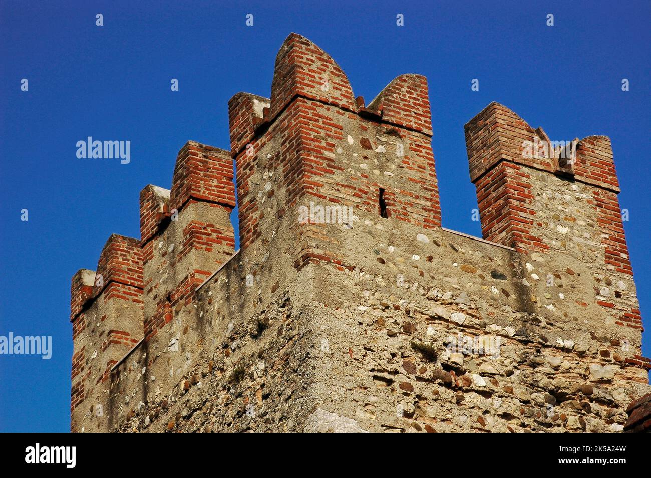 Merluzzi di coda di rondine, costruiti in mattoni, coronano una delle torri principali di un castello medievale, il Castello Scaligero o Rocca Scaligera, a Sirmione, in Lombardia. Costruito nel 1300, il castello prende il nome dalla famiglia della Scala, dinastia regnante di Verona, che dominava la zona all'epoca. È una delle fortezze scaligere meglio conservate. Foto Stock