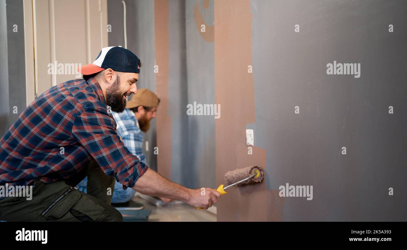 due uomini bearded con pittura a rullo dipingono le pareti facendo riparazioni. ristrutturazione, costruzione e concetto di casa. Banner Foto Stock