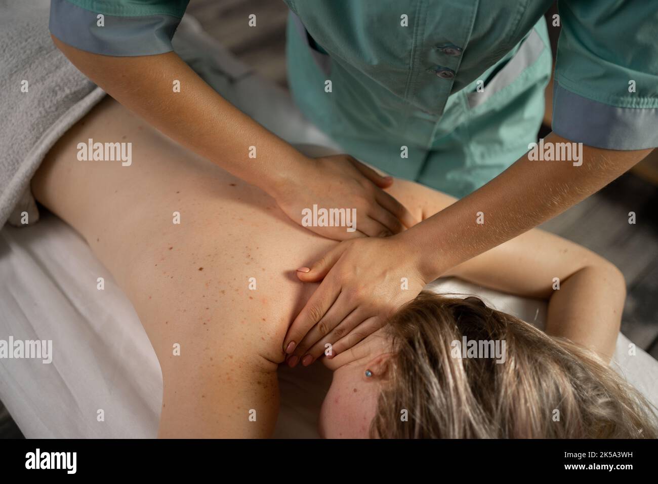 Vista dall'alto primo piano delle mani massaggiatrici che massaggiano il collo femminile nel salone termale Foto Stock