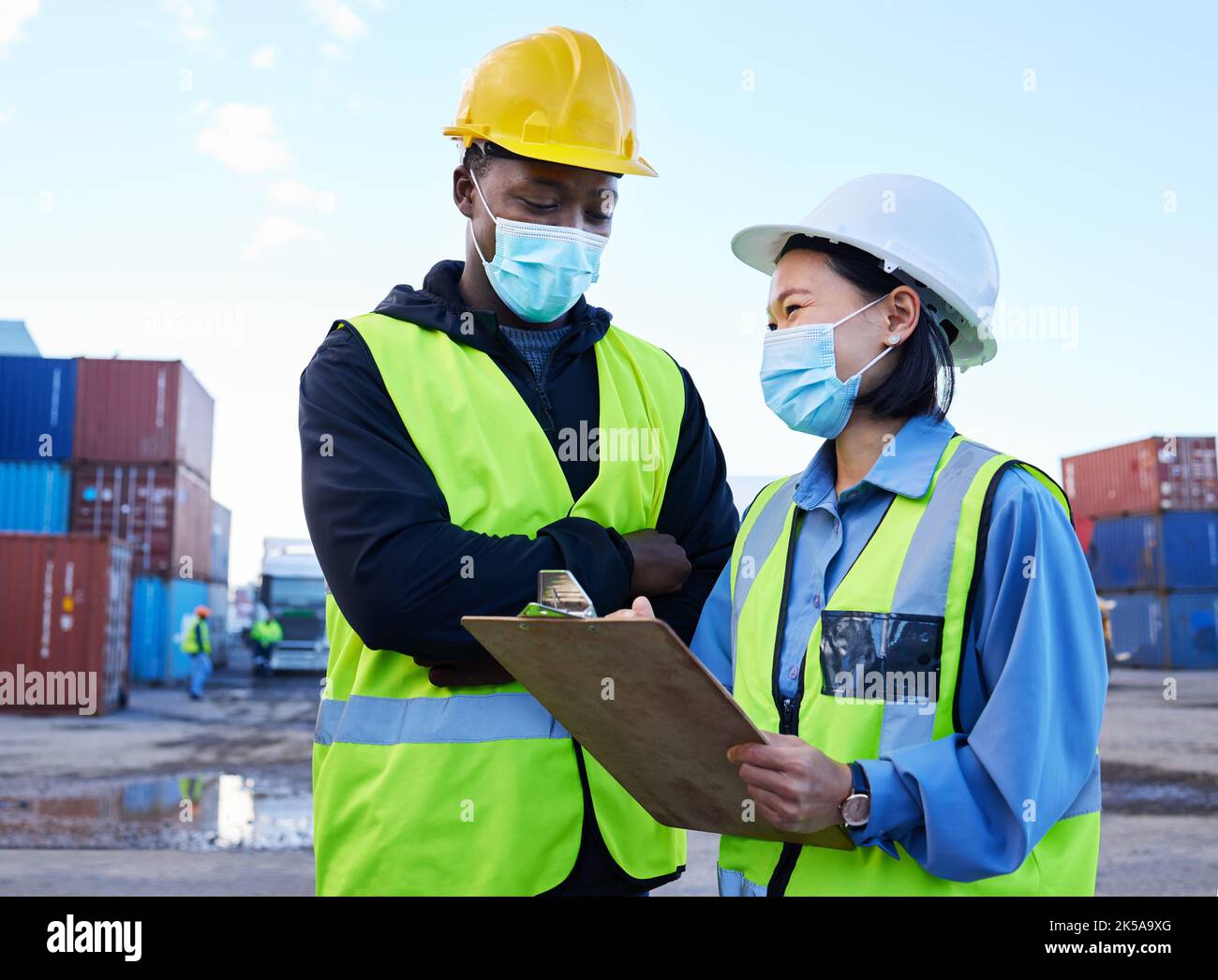 Logistica, spedizioni e team con maschera per la sicurezza di un vid con una lista di controllo per l'inventario del carico su un porto. Esportazione di consegne o gestione della catena di fornitura Foto Stock