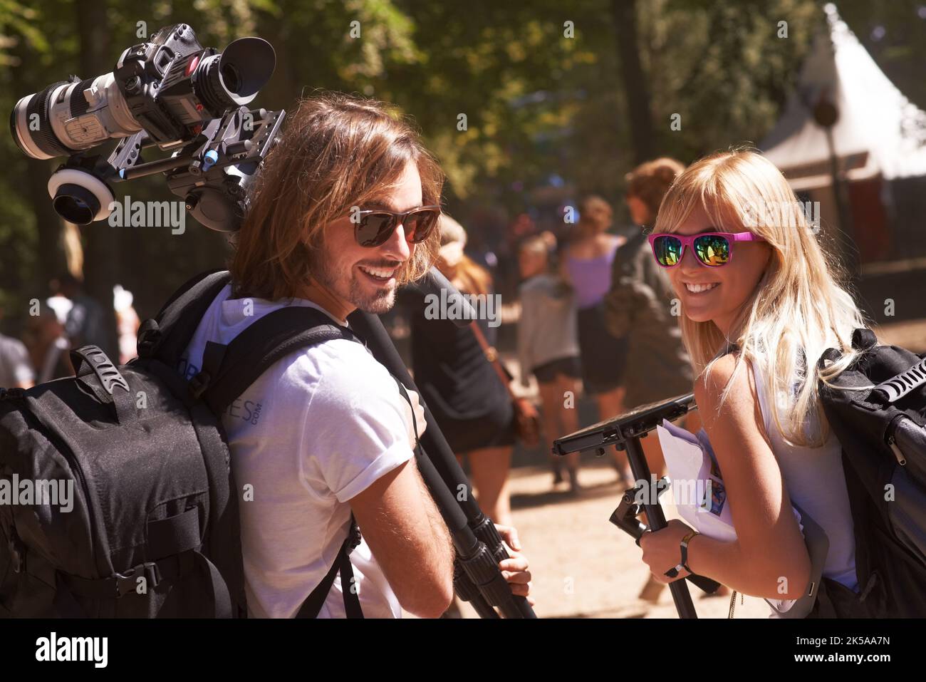 Fotografi di festival al lavoro. Vista posteriore di due fotografi sorridenti che guardano le spalle e camminano con l'attrezzatura nelle mani. Foto Stock
