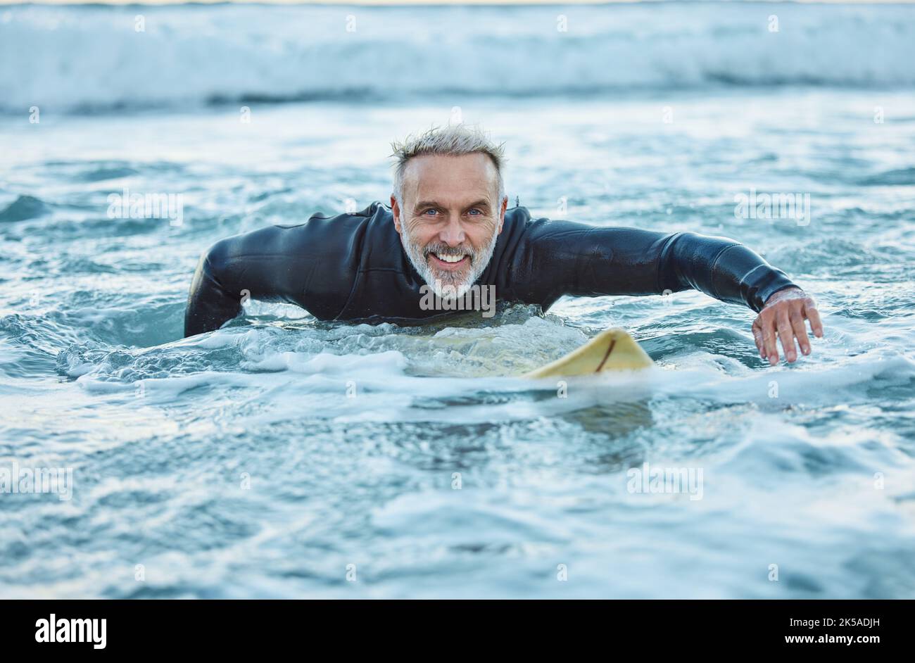 Uomo anziano, acqua e sport surfista su una spiaggia con sorriso formazione per fitness e salute o hobby all'aperto. Anziano maschio pagaiando in tavola da surf Foto Stock