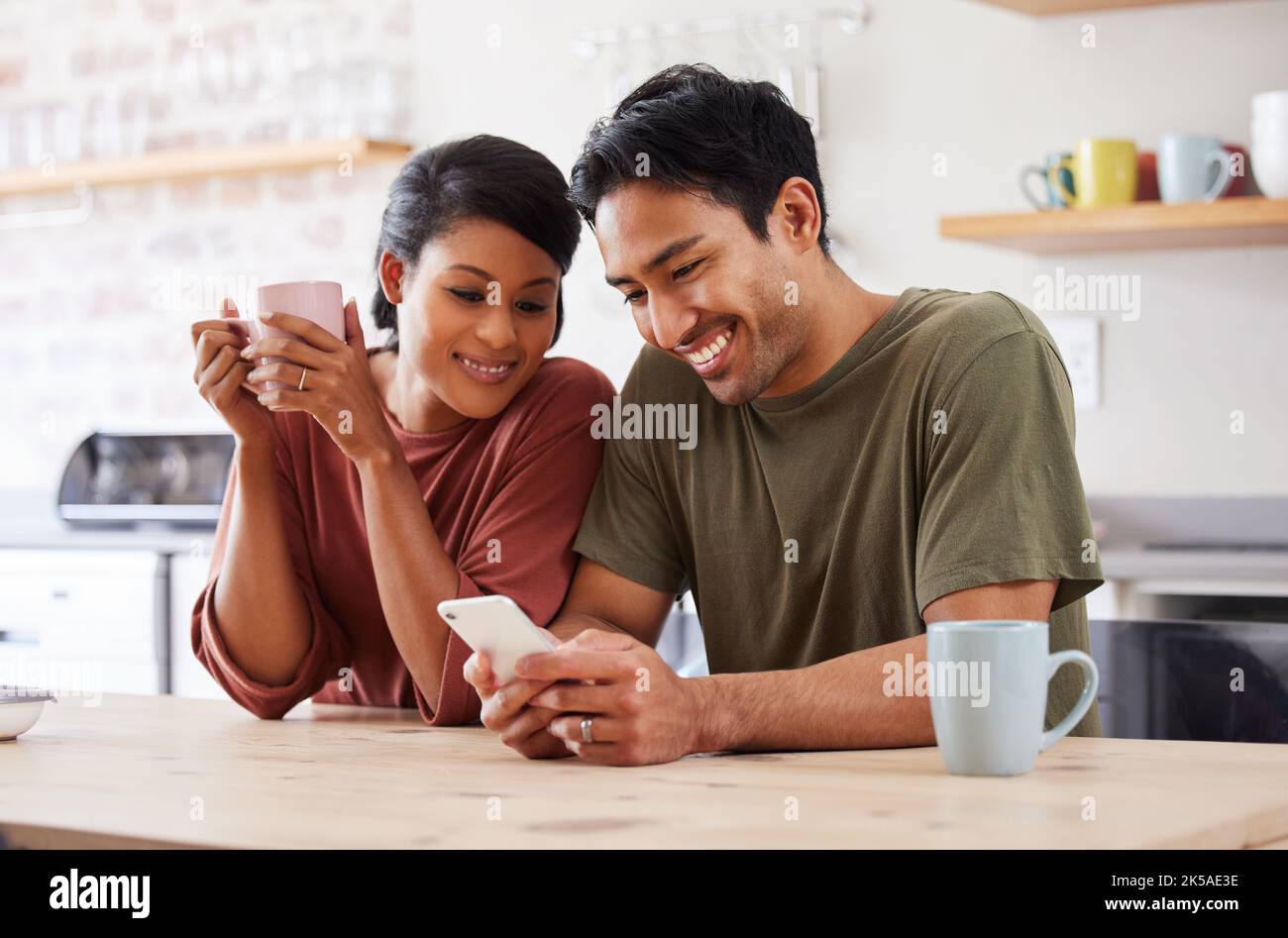Telefono, social media e coppia con un uomo e una donna nella cucina della loro casa insieme al mattino. Mobile, caffè e comunicazione con un Foto Stock