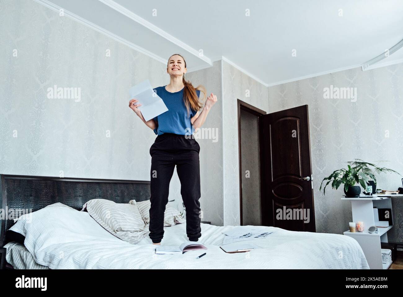Eccitato giovane donna allegra ha ricevuto una lettera, è assunta, saltando sul divano a casa, ottenendo le buone notizie, ritenendo la gioia, ballando, ridendo, fare Foto Stock