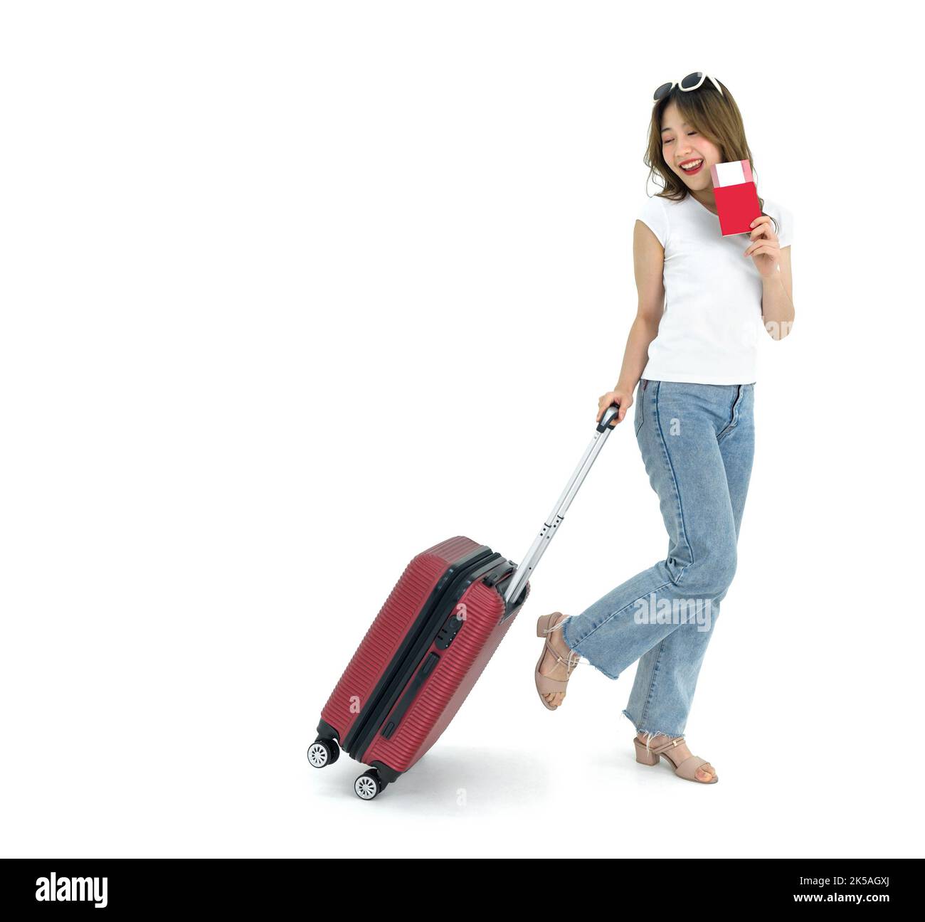 Giovane donna asiatica con t-shirt bianca e jean che trascina i bagagli mentre tiene in mano il passaporto di viaggio e il biglietto aereo. Ritratto su sfondo bianco con studi Foto Stock