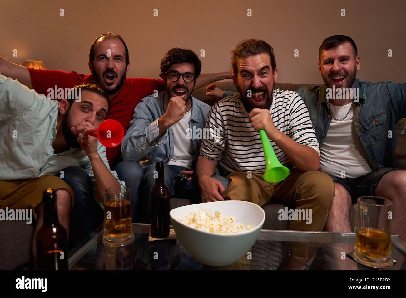 Un gruppo di amici maschi si è riunito per assistere a una partita di calcio, celebrando un punteggio gol, gridando felicemente. Foto Stock
