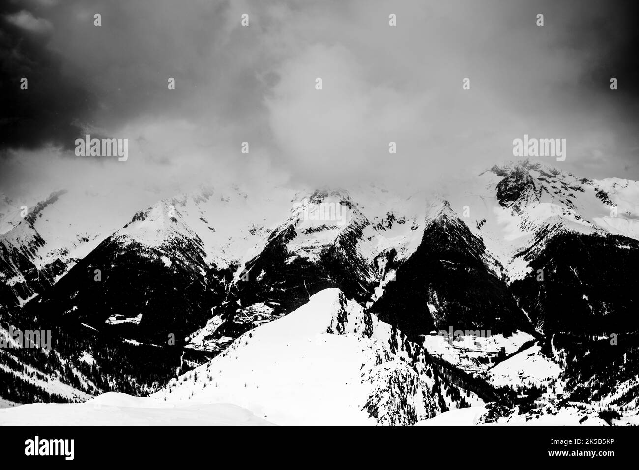 Una scala di grigi delle montagne innevate delle Alpi in Italia sotto un cielo nuvoloso Foto Stock