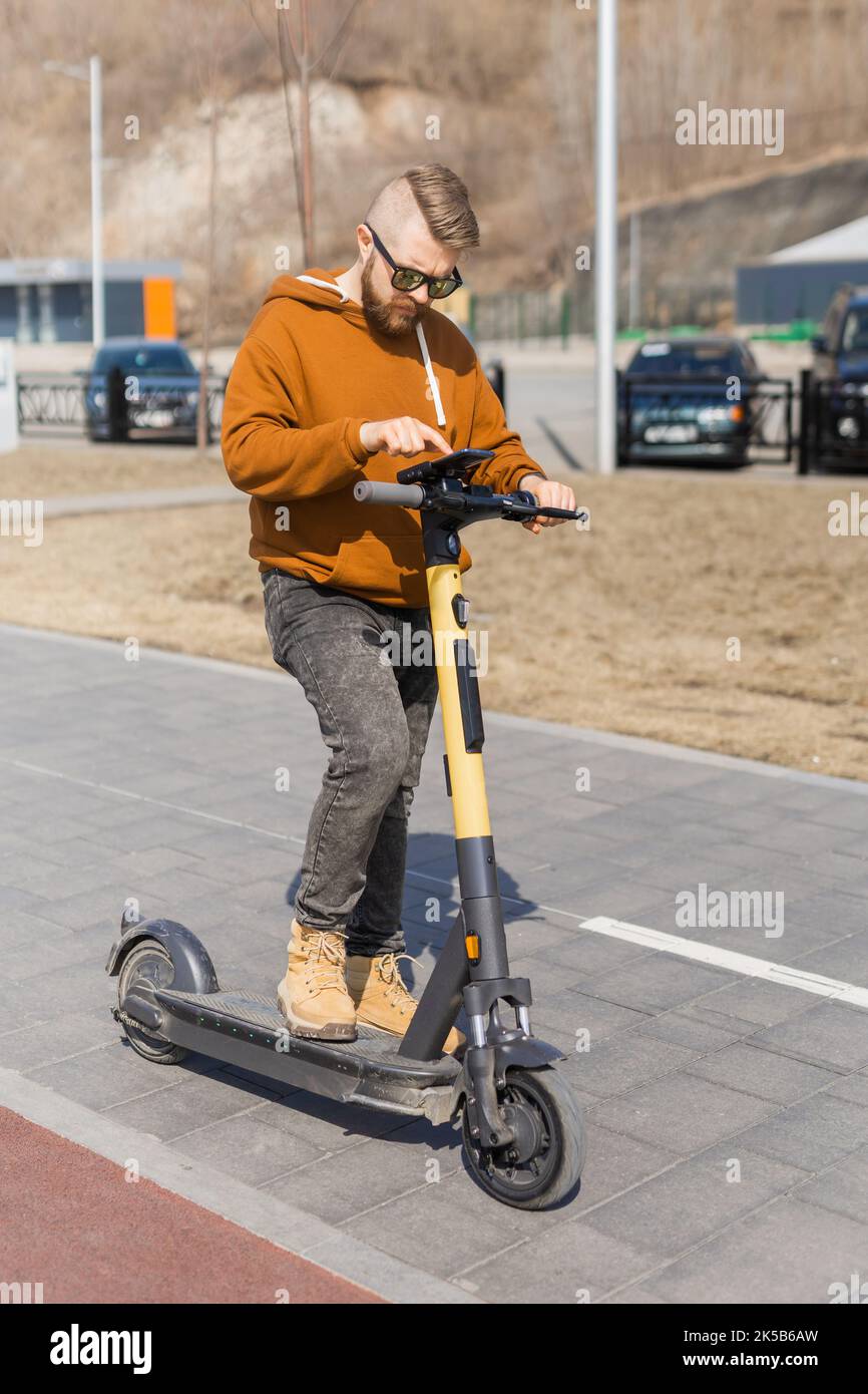 Uomo che utilizza lo smartphone dopo aver utilizzato uno scooter elettrico in città. Trasporto innovativo Foto Stock