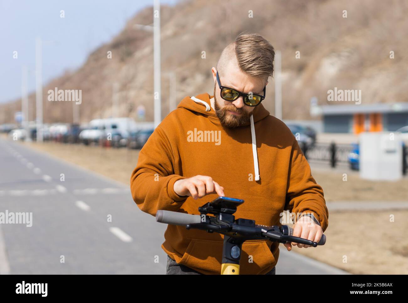 Uomo che utilizza lo smartphone dopo aver utilizzato uno scooter elettrico in città. Trasporto innovativo Foto Stock