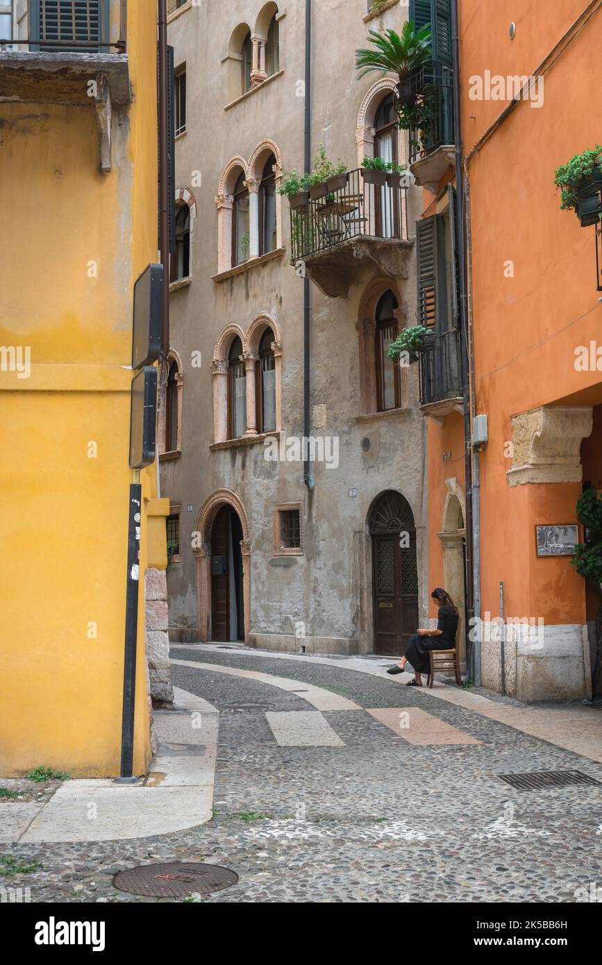 Città delle donne in Italia, vista di una giovane donna italiana seduta da sola in una strada tranquilla nel centro storico di Verona Foto Stock