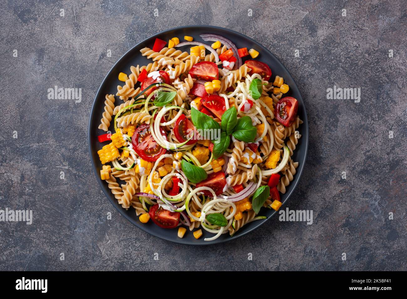 insalata di pasta sana con zucchine, mais dolce, pomodoro e basilico, pranzo vegetariano Foto Stock