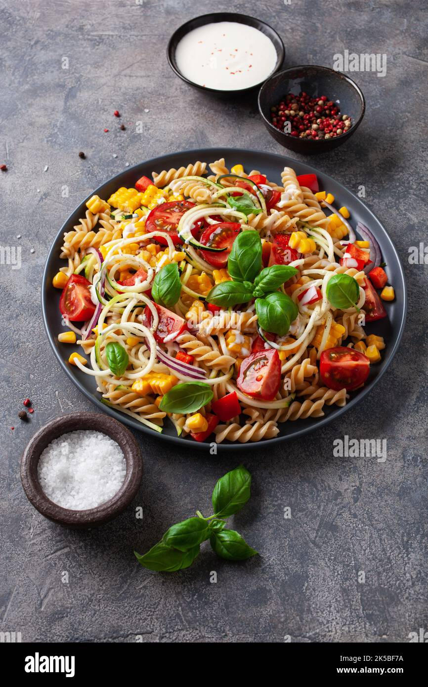 insalata di pasta sana con zucchine, mais dolce, pomodoro e basilico, pranzo vegetariano Foto Stock