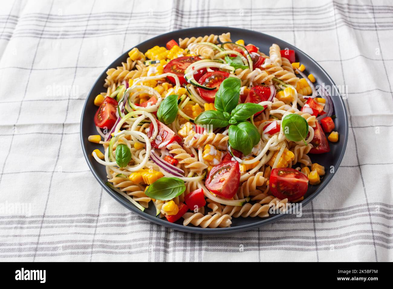 insalata di pasta sana con zucchine, mais dolce, pomodoro e basilico, pranzo vegetariano Foto Stock