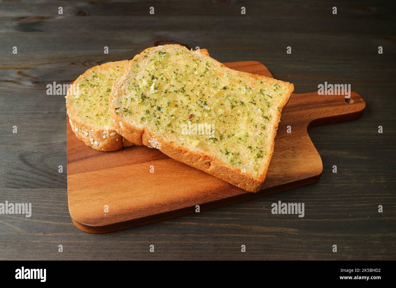Un paio di toast al burro all'aglio sul Breadboard servito sul tavolo di legno nero Foto Stock
