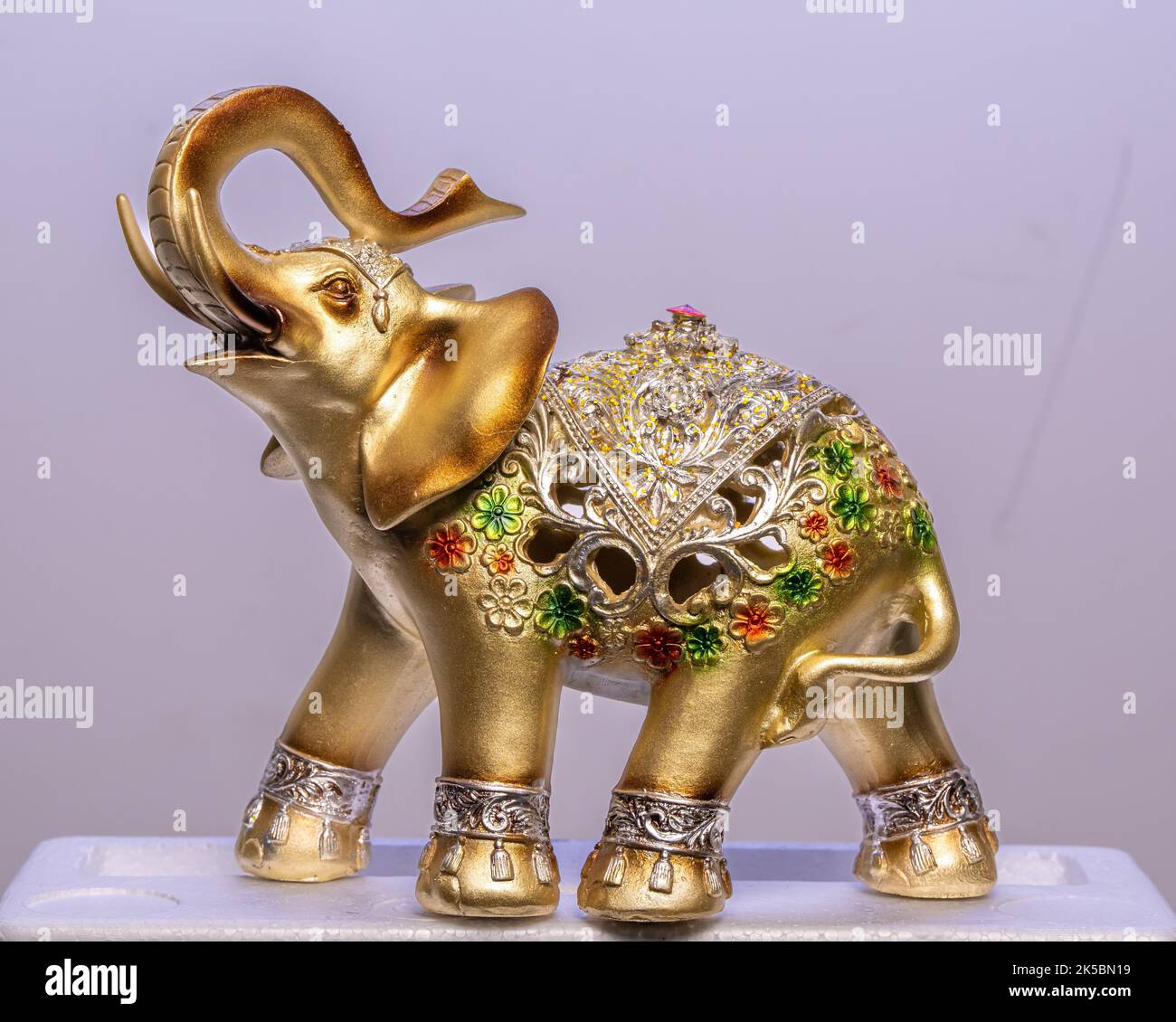 Un primo piano di una statua di elefante giallo dorato su sfondo bianco Foto Stock