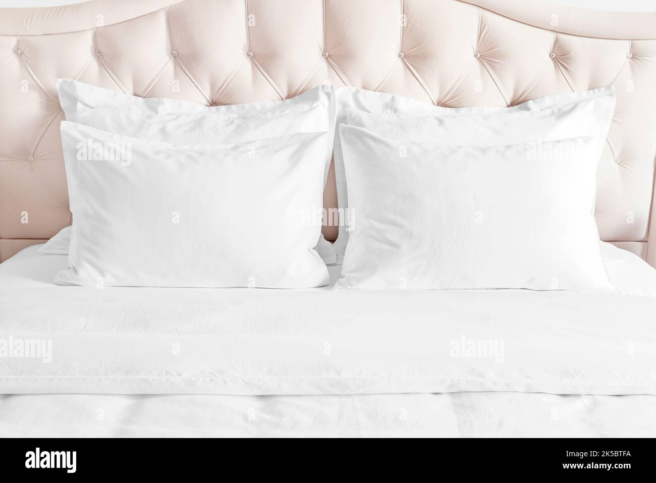 Camera da letto con letto e biancheria da letto bianca cuscini bianchi, piumone e piumone sul letto con testiera beige. Letto con cuscini bianchi e lenzuola pulite Foto Stock