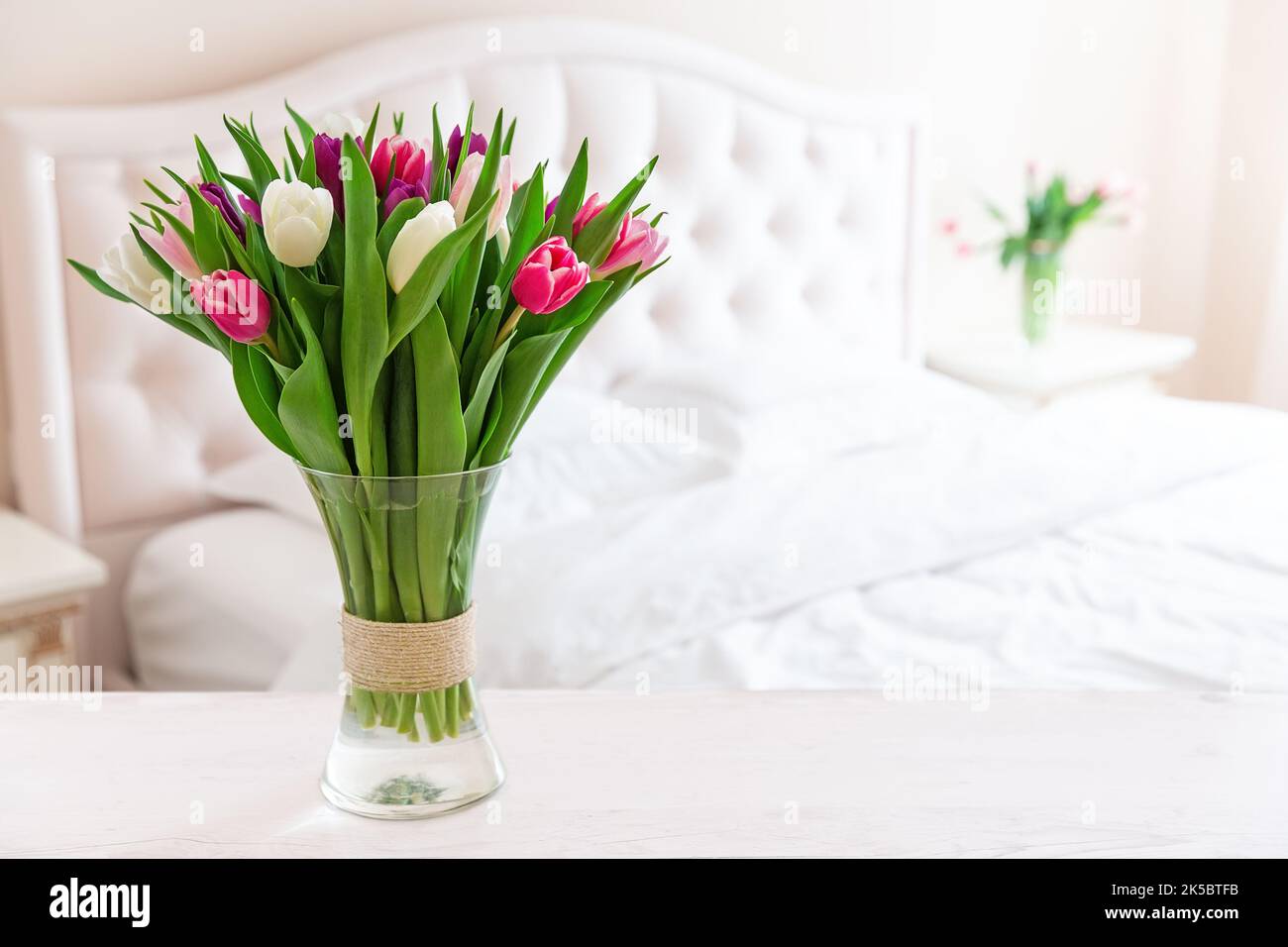 Le camere da letto sono dai colori tenui e chiari. Vaso di tulipani colorati in camera da letto luce accogliente interno. Interno di casa con tulipani rosa in un vaso su una camera da letto leggera sul retro Foto Stock