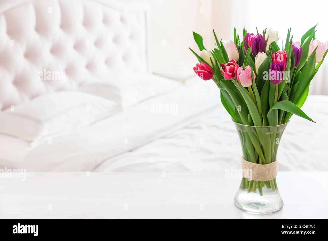 Le camere da letto sono dai colori tenui e chiari. Vaso di tulipani colorati in camera da letto luce accogliente interno. Interno di casa con tulipani rosa in un vaso su una camera da letto leggera sul retro Foto Stock