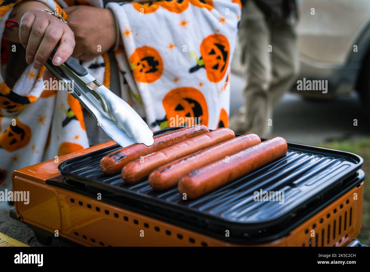 Donna cuoca hot dog su un campo all'aperto grill, concentrarsi sulla sua mano Foto Stock