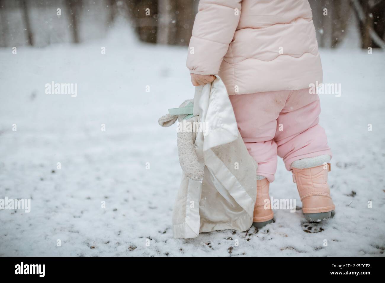 Giovane femmina nella neve che trascina un giocattolo di agnello farcito Foto Stock