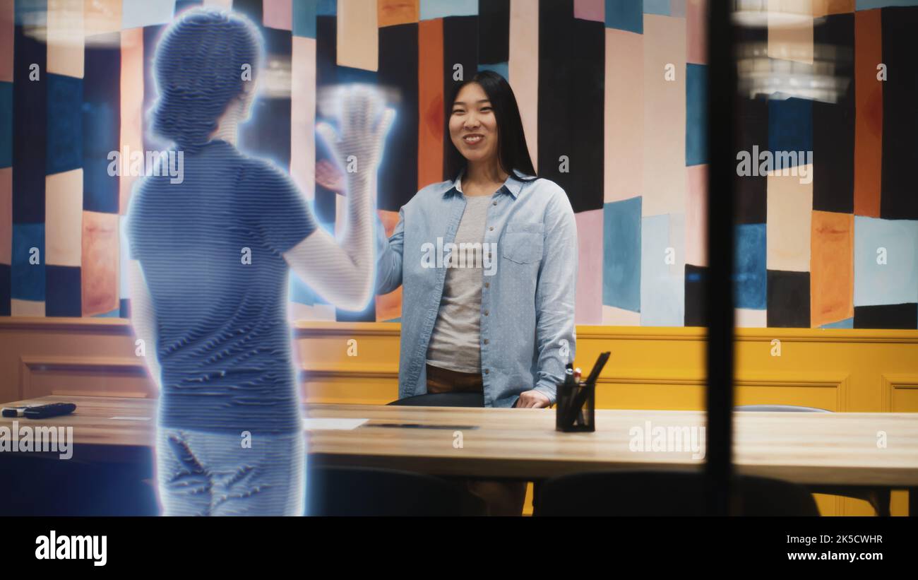 La donna asiatica parla alla chiamata con la sua amica utilizzando un software per la realtà aumentata. Ologramma della sua amica appare davanti a lei che riceve la chiamata. Effetti speciali VFX. Concetto di tecnologia futuristica. Foto Stock